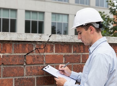 A consultant examining structural damage on a residential building with measuring tools.