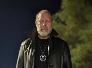 the founder standing outside at night in a black leather jacket and black low collared shirt.