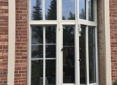 A friendly technician cleaning a large residential window with a squeegee on a sunny day.
