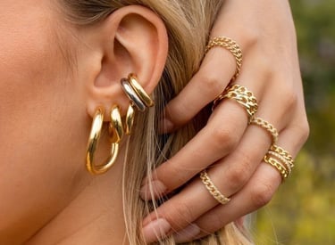 Mujer con grandes pendientes de aro dorados, un brazalete apilado y anillos de eslabones dorados