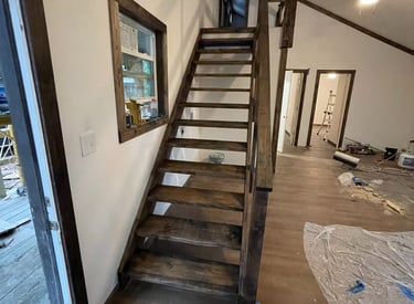 Custom dark wood staircase leading to a loft in a modern tiny house interior during construction.