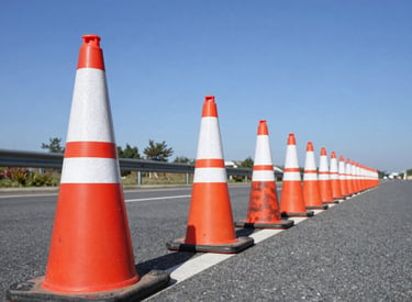 Traffic cones lined up along a freshly paved road under a clear sky.
