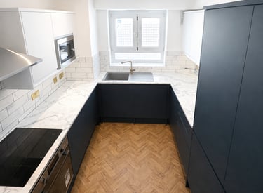 Modern kitchen with navy blue cabinets, white marble countertops, and herringbone wood flooring.