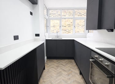Modern narrow kitchen featuring charcoal cabinets, white quartz countertops, and herringbone flooring.