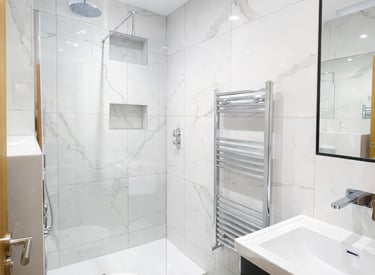 Modern bathroom with white marble tiles, walk-in shower, vanity unit, and heated towel rail.