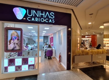 Modern Unhas Cariocas nail salon storefront in a bright shopping mall with professional manicurists.