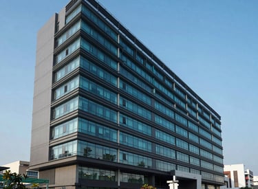 An exterior architectural photograph of a sleek, modern pharmaceutical research center in a South Asian / Indian urban setting, clear blue sky, palette of dark teal and slate grey.