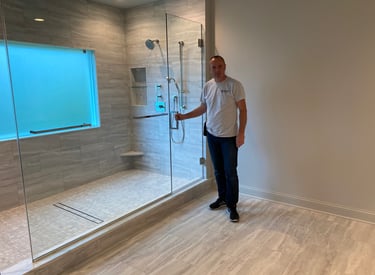 Wes contractor showing a newly installed frameless glass walk-in shower with gray tiles.