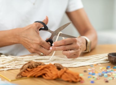 Una persona usando tijeras para cortar un cordón blanco de macramé para un proyecto de manualidades.