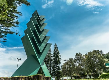Modern green geometric sculpture stands tall in a public park under a bright blue sky.