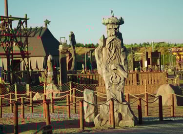 Tall stone Viking warrior statue at a Nordic-themed adventure park with wooden structures and ships.