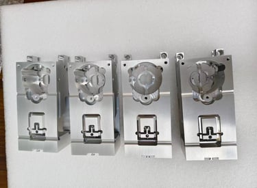 Four precision CNC machined aluminum industrial parts displayed on a white foam surface.