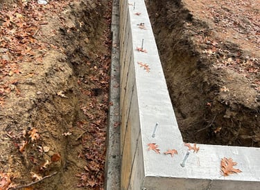 Poured concrete foundation wall with steel anchor bolts on a residential construction site.