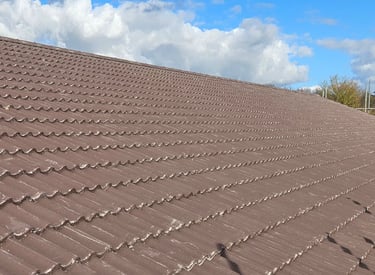 Durable brown concrete roof tiles installed on a residential home under a blue cloudy sky.