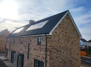 Modern brick house with rooftop solar panels installed on a dark tiled roof under a bright blue sky.