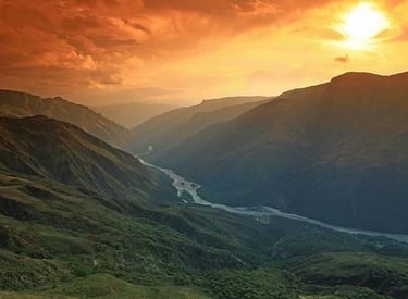 Golden sunset over a deep mountain valley with a winding river flowing through the canyon.