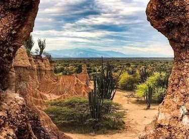 A scenic view of the Tatacoa Desert in Colombia framed by a natural rock window with cacti and red sand.