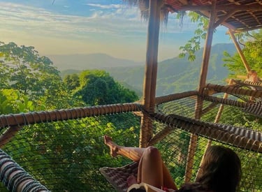 A woman relaxes in a net hammock at a tropical mountain eco-resort while reading a book.