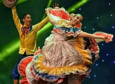 Couple performing a traditional Colombian Cumbia dance in vibrant folkloric costumes under green stage lights.