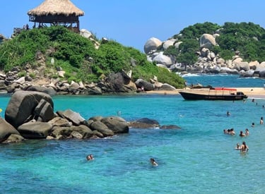 Tropical beach at Tayrona National Park in Colombia with clear turquoise water and a thatched hut on a rocky hill.
