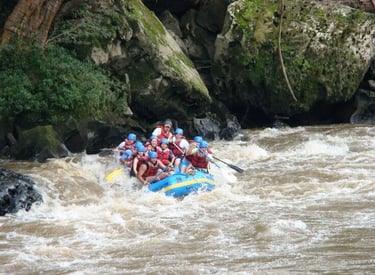 A group of people wearing helmets and life jackets white water rafting down a river with rocky banks.