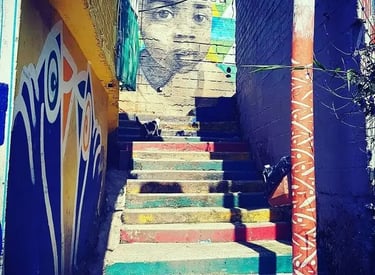 Vibrant street art mural of a child’s face overlooking colorful painted stairs in a narrow alleyway.