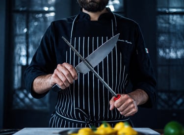 Chef sharpening a knife with crossed blade in a cinematic, moody setting