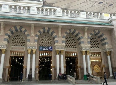 Grand entrance of Al-Masjid an-Nabawi in Medina with ornate arches and large umbrellas.