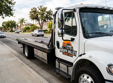 Street-level photo of a white flatbed tow truck featuring the logo of Jurupa Valley Towing Team,