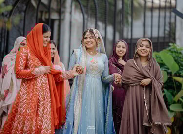 A smiling bride in a light blue embroidered Pakistani bridal dress walking with bridesmaids.