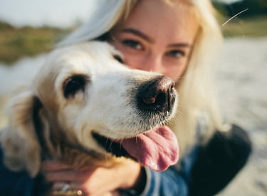 a woman with her dog in a blue jacket on the beach.