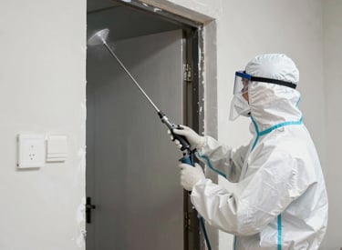 Professional painter in protective gear uses an airless sprayer to apply gray paint to a concrete block wall.