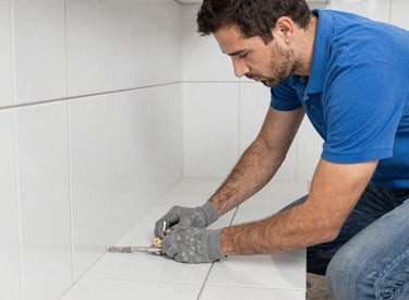 Professional painter in protective gear uses an airless sprayer to apply gray paint to a concrete block wall.