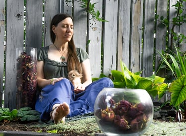 a woman sitting next to a pond surround by plants and roses holding a stuffed owl