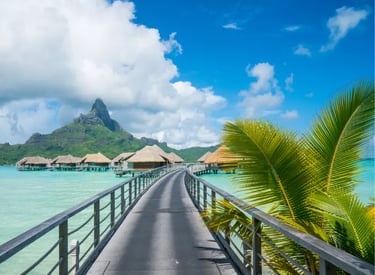 Luxury overwater bungalows in Bora Bora with a boardwalk over turquoise water and Mount Otemanu in the background.