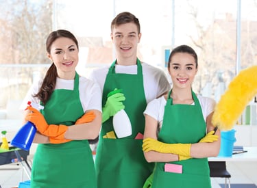 a group of people in green aprons holding cleaning supplies