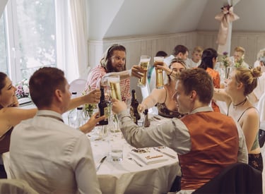 Hochzeitsgäste stoßen fröhlich mit Biergläsern am Tisch an. Authentische Eventfotografie von Just Perspectives.