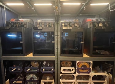 a shelf with a 4 bambu p1s printers. A bunch of filament rolls on the bottom of the shelves