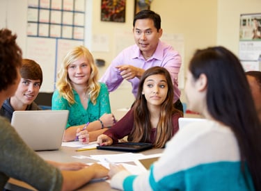 Students collaborating on laptops with teacher