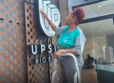 uma mulher limpa uma fachada ela está de camisa cinza com verde 