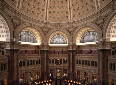 Interior view of a grand, circular library with a domed ceiling and rows of illuminated desks 