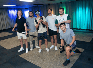 Group of young men, one man wearing a VR headset, one man holding an ice hockey stick