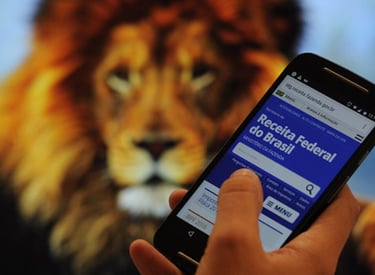 Pessoa segurando celular com site da Receita Federal aberto, ao fundo imagem de leão.