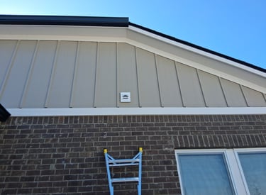 Board and batten style siding on gable end of a house above red brick.