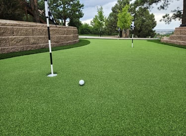 an artificial putting green area with fringe around it and a golf ball and cup and flag.