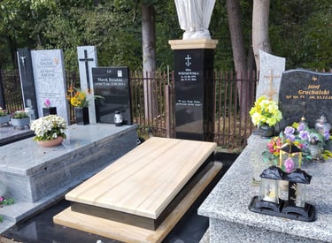 Polished granite tombstones and a white angel statue in a cemetery with floral tributes.