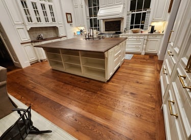 Luxury kitchen featuring wide plank heart pine hardwood floors and a large white center island with a wood countertop.