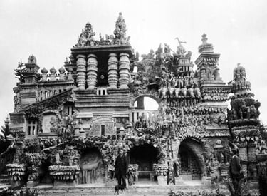Vintage black and white photo of Ferdinand Cheval standing before Palais Idéal, his intricate pebble stone palace.