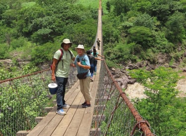 Roger Orozco, and a volunteer smile together as others cross a bridge over rocky terrain below.