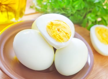 Hard-boiled eggs peeled and halved on a plate with fresh parsley and olive oil in the background.
